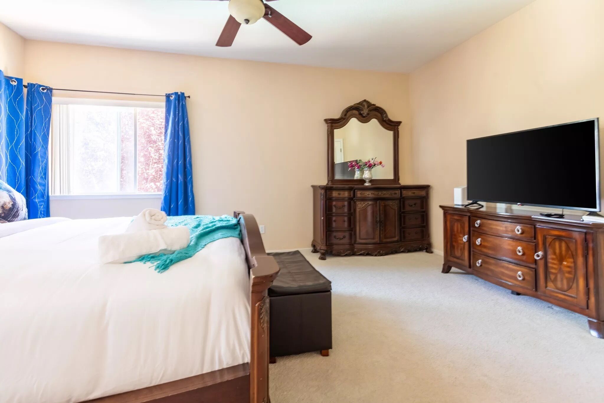 A bedroom with a bed, a dresser, a television, and a ceiling fan.