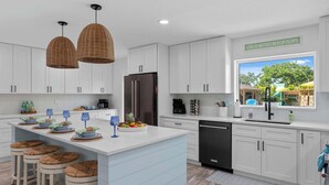A modern kitchen with white cabinets, a central island with stools, a refrigerator, and a window with a view of a playground. - Private Splash Pad, Pickleball, Htd. Pool, Hot Tub (Bradenton)
