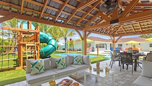 An outdoor patio area with a wooden pergola, a green slide, a pool, and a dining setup with outdoor furniture. - Private Splash Pad, Pickleball, Htd. Pool, Hot Tub (Bradenton)