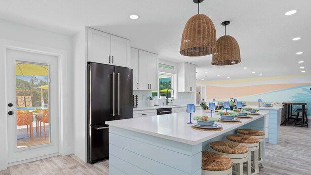 A modern kitchen with white cabinets, a black refrigerator, and a large island with stools. There are wicker pendant lights and a mural on the wall. - Private Splash Pad, Pickleball, Htd. Pool, Hot Tub (Bradenton)