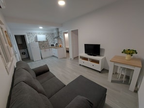 A modern living room with a sofa, a TV on a white stand, and a small table with a plant.