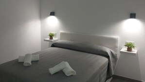 Une chambre moderne avec un lit, deux tables de chevet ornées de plantes et des lampes fixées au mur.