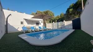 Une piscine à l’eau bleue, entourée de gazon synthétique, avec des chaises longues bleues.