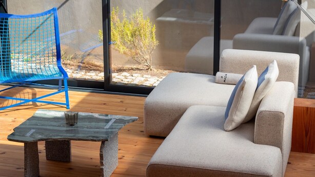 A modern living room with a stone coffee table, a blue chair, and a beige sofa with pillows.
