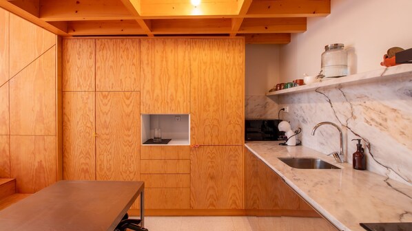 A compact kitchen with wooden cabinetry, a marble countertop, and a small window.