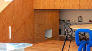 A modern kitchen with wooden cabinetry, a marble countertop, and a blue chair.