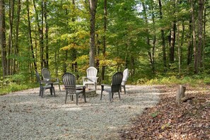 Entorno boscoso con zona de grava y cuatro sillas Adirondack dispuestas alrededor de una mesa central.