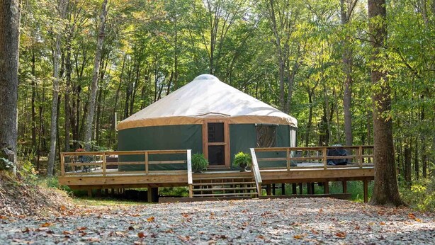 Una struttura in stile yurta con veranda in legno e ingresso coperto, immersa in una foresta.