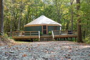 Una estructura tipo yurt con terraza de madera y entrada cubierta, rodeada de un bosque.