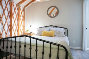 Un dormitorio con cama, mesita de noche, espejo y pared de celosía de madera.