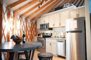 Una cocina con vigas de madera, armarios blancos, un refrigerador de acero inoxidable, un microondas y un lavamanos.