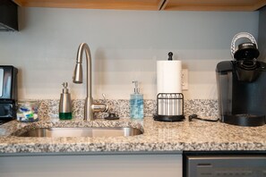 Una cocina con grifo de acero inoxidable, cafetera, dispensador de jabón y un tarro de aperitivos.