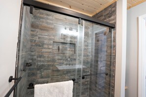 Ducha con puerta de vidrio, toallero y techo de madera.