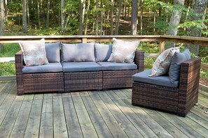 Un conjunto de sofá y sillones de mimbre sobre una terraza de madera con barandilla de madera.
