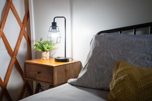 Una cama con un cojín estampado, una mesita de noche con una lámpara y una planta.