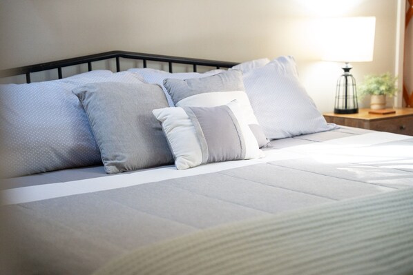 Una cama bien hecha con cabecera, varios almohadones y una lámpara de noche.