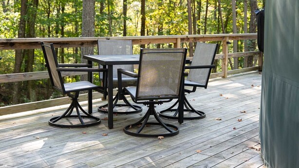 Eine Terrasse mit Tisch und Stühlen, umgeben von einem Holzgeländer, mit Blick auf einen Wald.