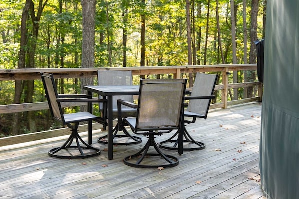 Una terraza con mesa y sillas, rodeada por una baranda de madera, con vista a un bosque.