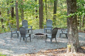 Un paisaje forestal con una hoguera y cuatro sillas Adirondack dispuestas alrededor.