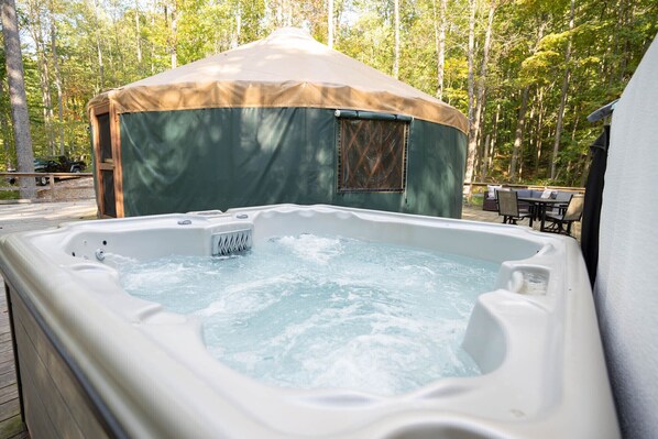 Un jacuzzi con plataforma de madera, zona cubierta y fondo boscoso.