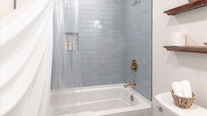 A bathroom with a bathtub, shower, and toilet. There is a towel rack with towels and a basket on the wall.