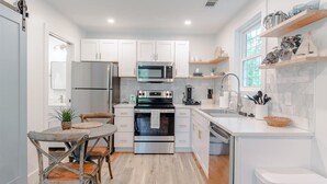A modern kitchen with white cabinets, stainless steel appliances, and a wooden dining table.