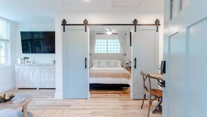 A modern bedroom with a bed, a desk, and a chair. There is a sliding door leading to another room.