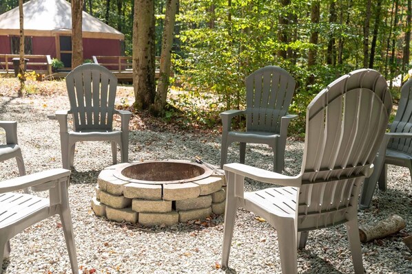 Espace extérieur aménagé avec des chaises Adirondack disposées autour d’un foyer en pierre.