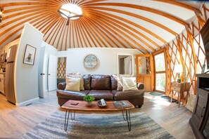 A cozy living room with a leather sofa, a coffee table, and a wooden ceiling. - Arbor Ridge Yurt- Hocking Hills Yurts and Cabins (Laurelville)