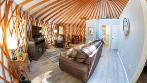 A cozy interior with a wooden ceiling, a fireplace, a sofa, and a dining area. - Arbor Ridge Yurt- Hocking Hills Yurts and Cabins (Laurelville)