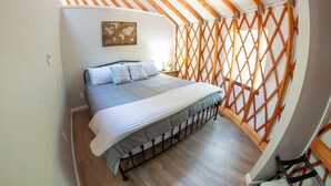A bedroom with a bed, a world map artwork, wooden beams, and a wooden floor. - Arbor Ridge Yurt- Hocking Hills Yurts and Cabins (Laurelville)