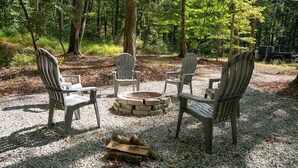 A campsite with four Adirondack chairs around a stone fire pit, surrounded by gravel and trees. - Arbor Ridge Yurt- Hocking Hills Yurts and Cabins (Laurelville)
