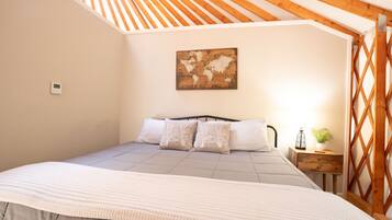 A bedroom with a sloped ceiling, a bed with a headboard, a world map artwork, a thermostat, and a nightstand with a lamp and a plant.