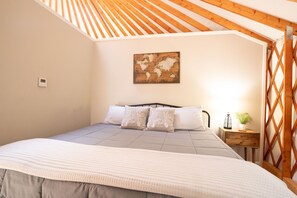Une chambre avec un plafond en pente, un lit doté d’une tête de lit, une œuvre d’art représentant une carte du monde, un thermostat et une table de chevet avec une lampe et une plante.