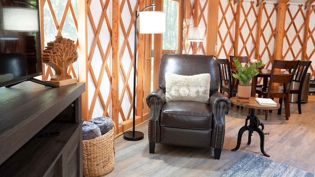 A cozy room with a leather armchair, a wooden table with a plant, and a TV on a wooden stand. - Arbor Ridge Yurt- Hocking Hills Yurts and Cabins (Laurelville)