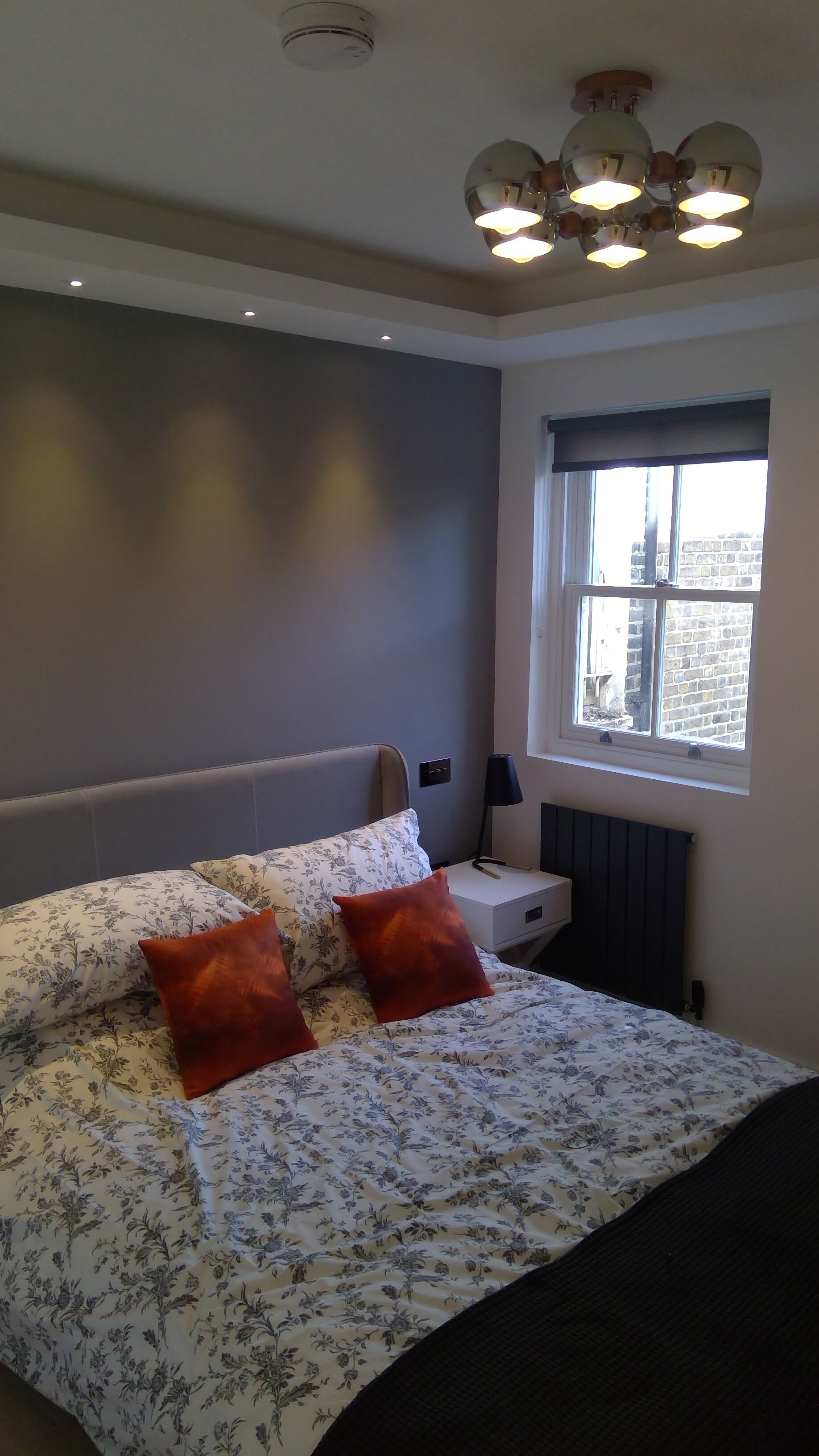 Un dormitorio con cama, mesita de noche, lámpara y ventana.