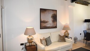 A modern living room with a white sofa, two side tables with lamps, a painting on the wall, and a brick accent wall.