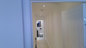 A narrow hallway leading to a bathroom with a toilet, sink, and mirror.