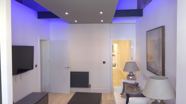 A modern living room with a flat-screen TV, a sofa, a lamp, and a radiator.
