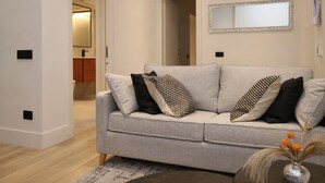 Un salon avec un canapé gris, des coussins à motifs noir et blanc, un miroir au mur et un vase contenant des plantes séchées sur une table d’appoint.