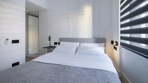 Una habitación de hotel moderna con una cama grande, una mesita de noche, un teléfono en la pared y una ventana con persianas.