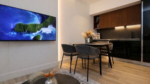 Une cuisine moderne avec un téléviseur à écran plat fixé au mur, un coin repas avec une table ronde et des chaises, et un vase décoratif posé sur le sol.