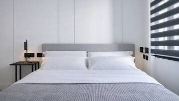 Une chambre d’hôtel moderne avec un grand lit, une table de chevet avec une lampe et une fenêtre équipée de stores.
