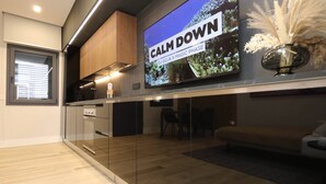 A modern kitchen with a built-in oven, a dining area with a bench, and a large flat-screen TV displaying 'CALM DOWN DJ GOJA X MAGIC PHASE'. - Suite Monte Nero · Renovated 1BR in Central Olbia with King Bed · Modern Style (Olbia)