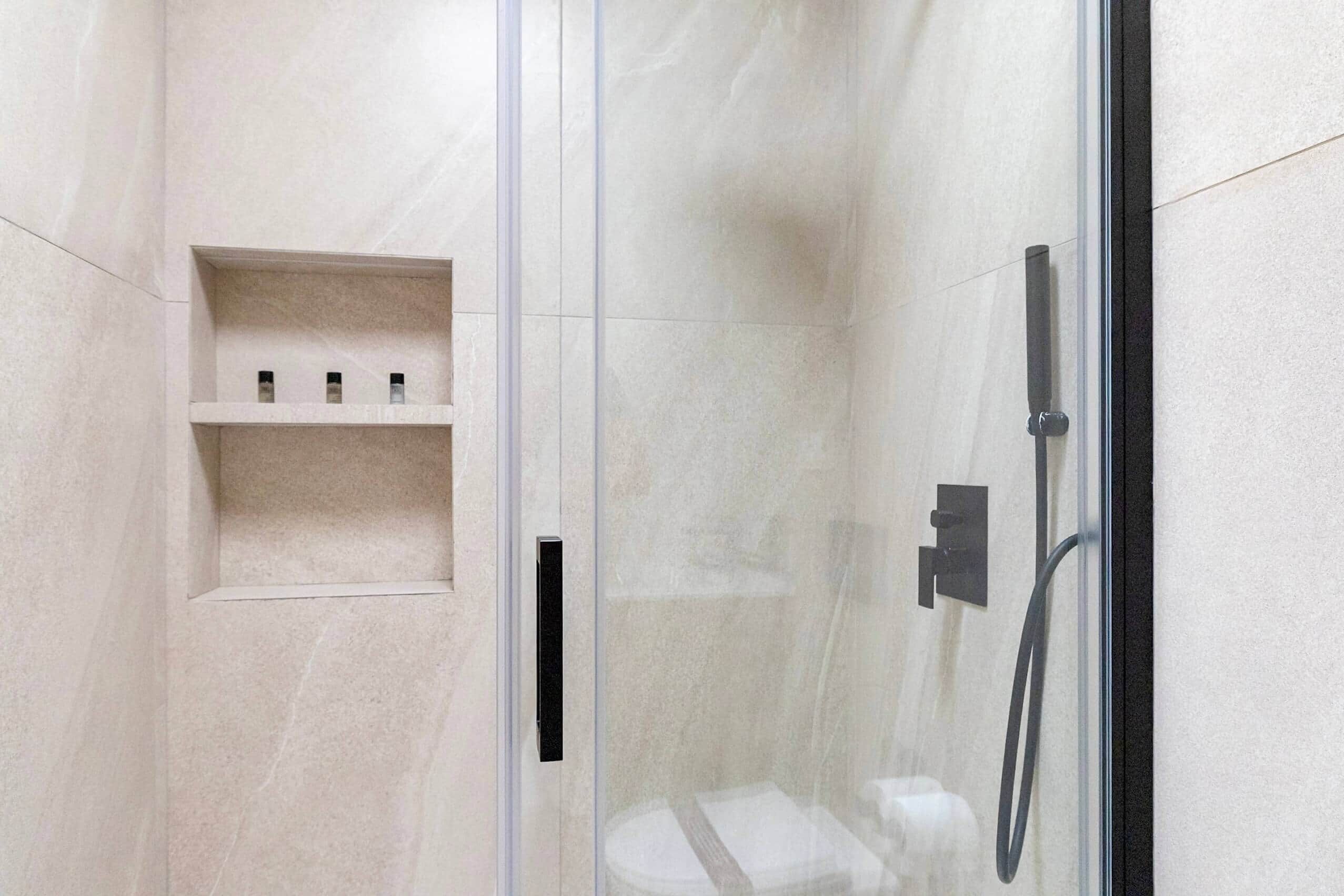 A modern shower with a glass door, a shelf with toiletries, and a handheld showerhead.