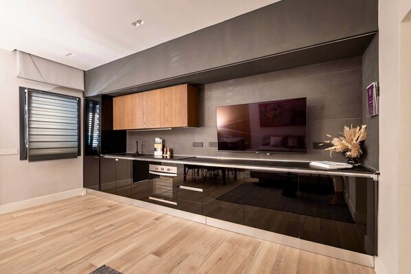 A modern kitchen with a built-in oven, wooden cabinets, and a large flat-screen TV.