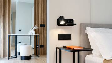 A modern bedroom with a grey sofa, a small black table with a book, a wall-mounted lamp, and a wooden panel wall.