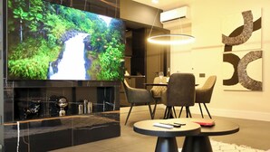 Una sala de estar moderna con un televisor de pantalla plana grande, un comedor con sillas y una mesa de centro negra.