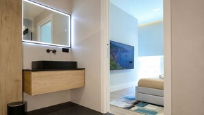 A modern bathroom with a wooden vanity, a mirror with integrated lighting, a black sink, and a black trash bin. - Cavour Suites 31, Olbia Old Town Duplex, King Bed, Office, Gated Parking (Olbia)