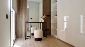 A modern interior with a wooden floor, a glass door, a black-framed table, and a white vase with dried plants.